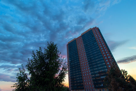Street view of an ordinary brick high-rise building against the background of the evening sky in Russia. Trees are visible in the foreground.の写真素材