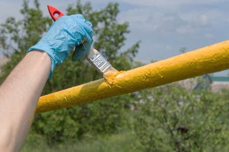 gloved hand paints the pipe in yellow in the gardenの写真素材