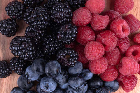 Unmixed piles of blueberries, blackberries and raspberries laying on wooden surfaceの写真素材