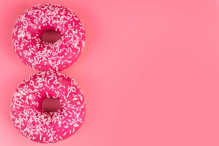Top view on two pink donuts  with white sprinkles laying close to each other on one side of a photoの写真素材