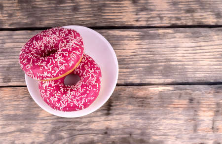 Top view of two pink glazed donuts laying on white plate standing on wooden background of gra planksの写真素材