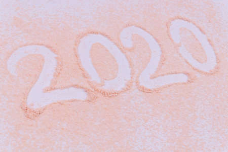 Close up view on inscription 2020 made of a finger trace on pale orange sand