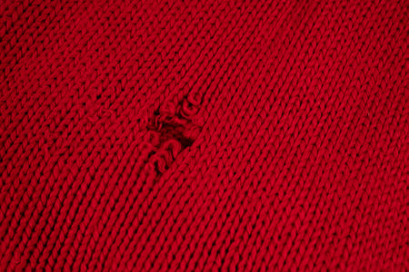 there is a hole in the knitted red fabric due to the torn thread