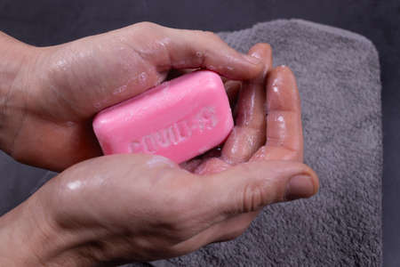 two wet hands are holding pink soap, and against the background is a gray towel