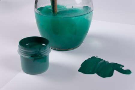 an open green jar of gouache, a few strokes on the surface nearby, and against the background of a jar of water and gouache mixedの写真素材