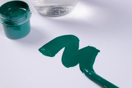 side view of a smear of green color and next to an open jar of green gouache, against the background of a transparent jar of waterの写真素材