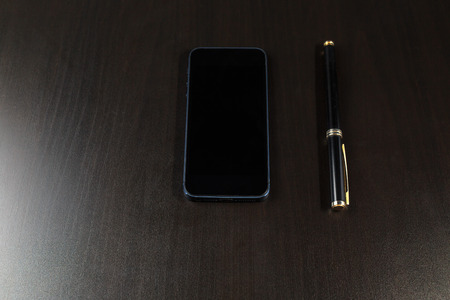 Black phone and a black fountain pen lying on a black wooden table.の写真素材