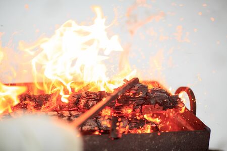 Hand with poker adjusts the coals in the brazier. Lighting the barbecue in the backyard in the...