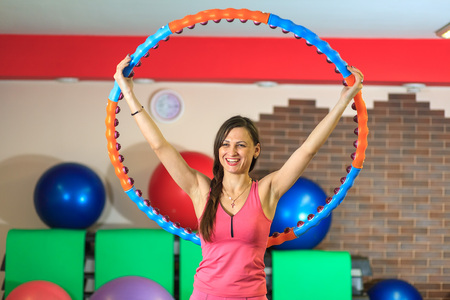 Young beautiful white girl in a pink sports suit does physical exercises with a hoop at the fitness center. Interior of fitness club for background.の写真素材