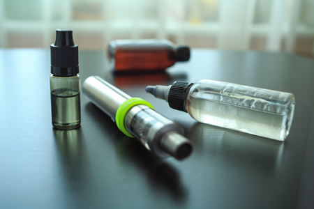 The electronic cigarette, a jar with the flavor and the liquid for steaming lie on a black table for background.の写真素材