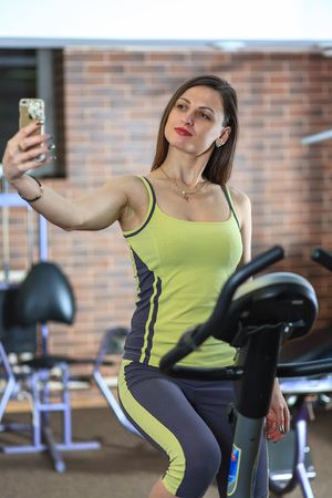 Young beautiful white girl in a yellow and gray sports suit is engaged on a stationary bike in the fitness club.の写真素材