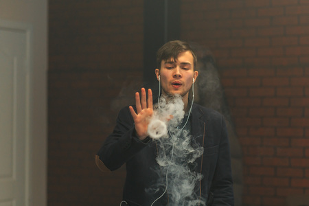 Young handsome white guy let rings out of steam. Vaping.の写真素材