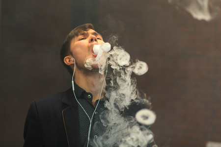 Young handsome white guy let rings out of steam. Vaping.の写真素材