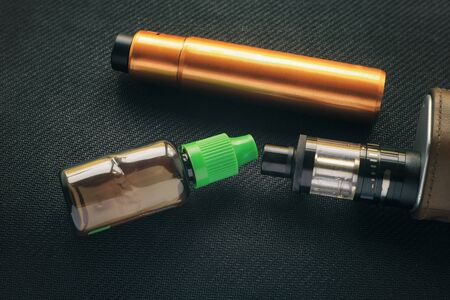 Vape. Bottle with e-liquid and nikotine and electronic cigarette mod on black textile. Personal...