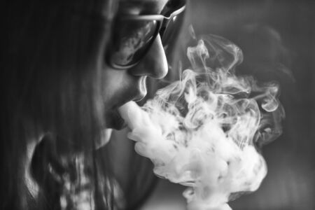 Vape. Young handsome white girl in sunglasses is admiting puffs of steam from the electronic...