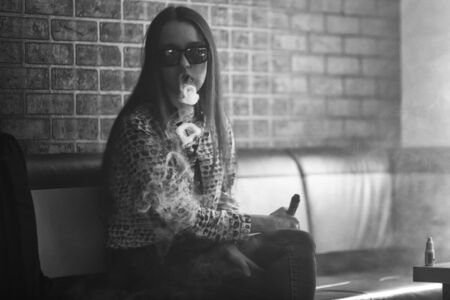 Vape. Young handsome white girl in sunglasses is admiting puffs of steam from the electronic cigarette. Vaping. Teenager. Black and white photo.の写真素材