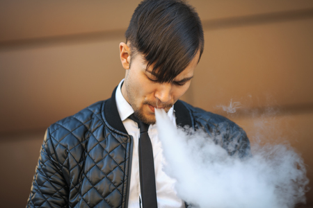 Vape man. Portrait of a handsome young white guy with modern haircut vaping an electronic cigarette...