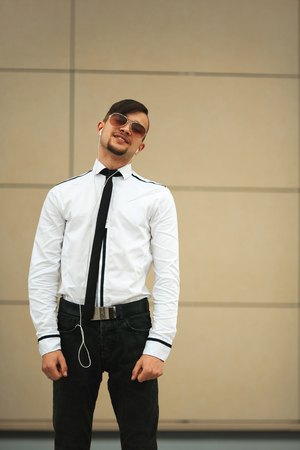 Portret of a handsome young white guy with modern haircut in aviator sunglasses and headphones opposite modern background.の写真素材