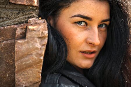 Portrait of young pretty white girl with black hair and in black clothes posing near the old stone wall.の写真素材