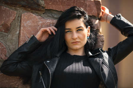 Portrait of young pretty white girl with black hair and in black clothes posing near the old stone wall.の写真素材