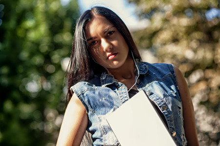 Young pretty brunette girl with the tablet and listening to music on the street in summer.