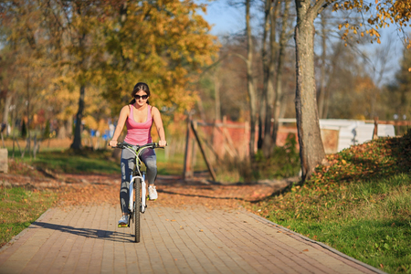 Young beautiful girl in sportswear stands next to a bicycle on the street in the park in autumn.の写真素材