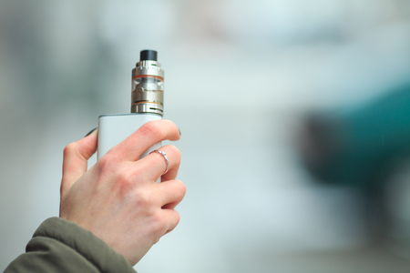Vape. Female white hand with electronic cigarette. Vaping on the street.の写真素材