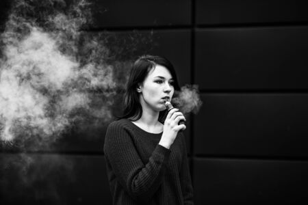 Vaping teenager with problem skin. Young pretty caucasian girl in a jacket smoking electronic...