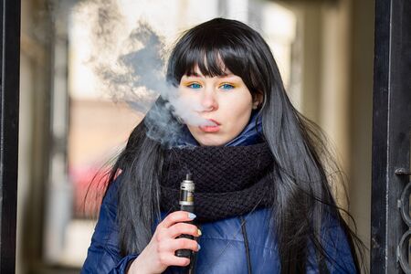 Vape teenager. Young pretty white caucasian brunette girl with blue eyes and in a blue jacket...