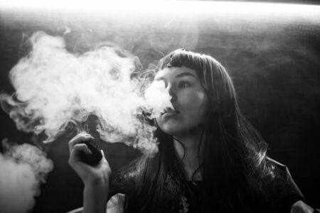 Vaping teenager. Young pretty white caucasian teenage brunette girl with problem skin smoking an...