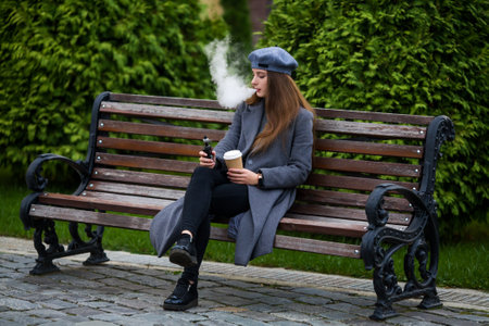 Vaping teenager. Young pretty white caucasian teenage girl in gray beret smoking an electronic...