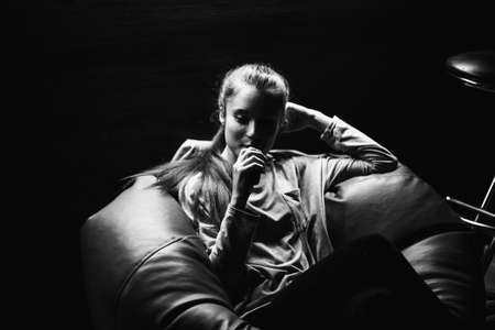 Vaping teenager. Young pretty white caucasian teenage girl with problem skin smoking an electronic cigarette indoors. Life-threatening bad habit. Vape activity. Black and white. Close up.の写真素材