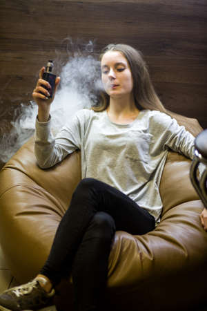 Vaping teenager. Young pretty white caucasian teenage girl with problem skin smoking an electronic...
