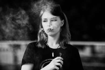 Vape teenager. Young pretty white caucasian girl with glasses on her head an electronic cigarette on the street in the summer. Deadly bad habit. Black and white.の写真素材
