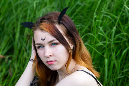 Young beautiful witch in black dress conducts a ceremony in a green forest on a summer day. Modern...