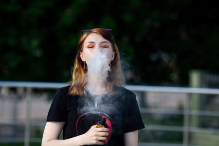 Vape teenager. Young pretty white caucasian girl with glasses on her head an electronic cigarette on...