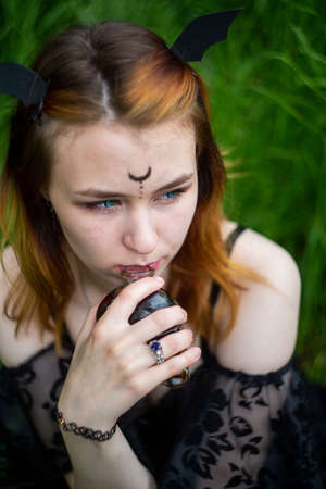 Young beautiful witch in black dress conducts a ceremony in a green forest on a summer day. Modern...