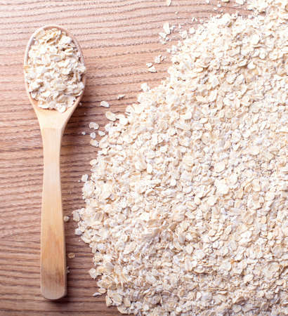 Heap of organic oatmeal, oat flakes with wooden spoon on a wooden backgroundの写真素材