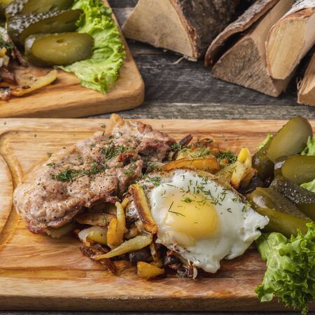 Fried pork meat with fried potatoes, eggs and salted cucumbersの写真素材