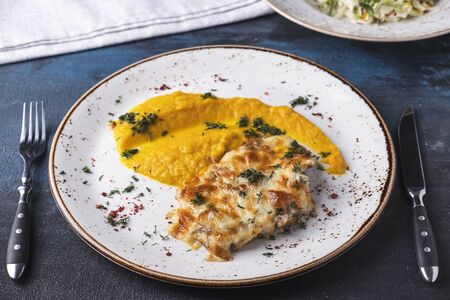 Delicious baked chicken under cheese with carrot puree on a plate served with fork and knifeの写真素材