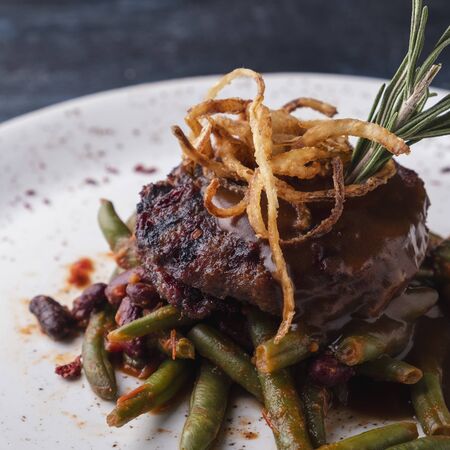 Delicious chopped meat steak with sauce and onion chips on a plateの写真素材