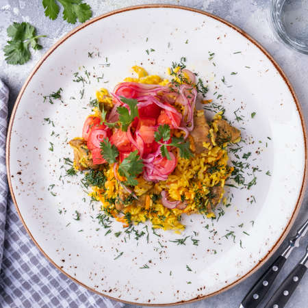 Top view of pilaf with meat, tomatoes and onions on a plate.