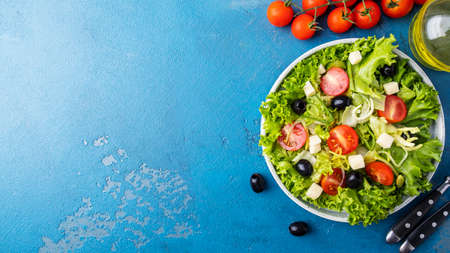 Lettuce, cheese, olives, onion and cherry tomatoes on a plate. Healthy and diet food concept. Top view, text spaceの写真素材