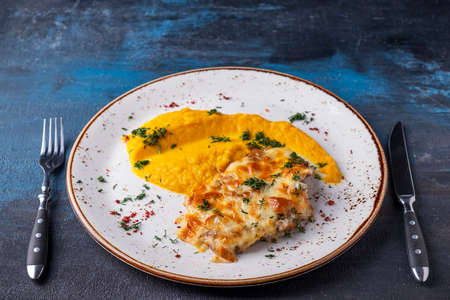 Baked chicken under cheese with carrot puree served with fork and knife.の写真素材