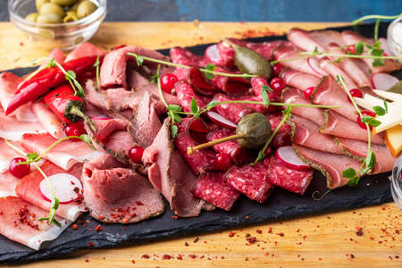 Various of meat on a black stone background. Assortment of ham, salami, sausages and prosciutto. Meat on a board. Closeupの写真素材