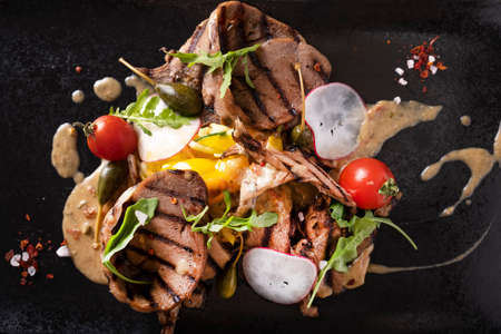 Griiled beef tongue with vegetables and sauce. Top view. Closeup