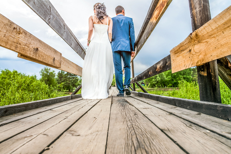 A couple of people in wedding clothes walking on a wooden bridge, rear viewの写真素材