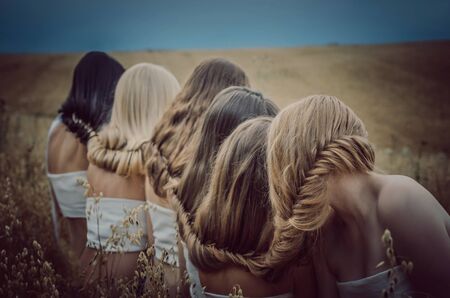 Girls blondes, redheads and brunettes closed hair in summer fieldの写真素材