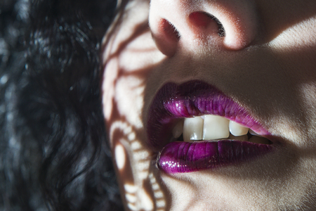 lips with purple lipstick and black hair closeup shadow through the lightの写真素材