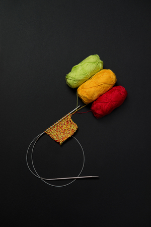 balls of yarn red green and yellow on a black background and knitting needles verticalの写真素材